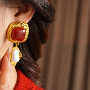 Close-up of vintage square red gemstone earrings with baroque pearls worn by a model