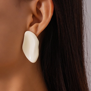 Close-up of model wearing cream wavy geometric earrings with a glossy finish