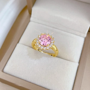 Détails d'une bague dorée ornée d'une pierre rose ronde entourée de petits diamants