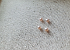 Detail of four round pink-purple pearls with natural luster on white fabric background