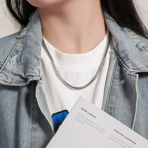 Close-up of a sleek silver snake bone chain necklace worn by a model in casual style