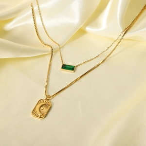 Double-layered gold necklace with green gemstone and moon relief pendant on silk fabric