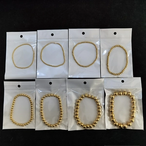 Multiple sizes of gold beaded elastic bracelets in packaging on a black background