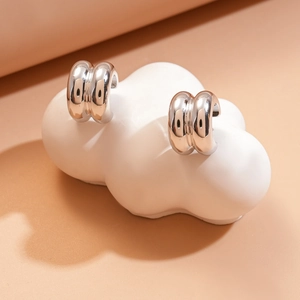 Macro view of silver double-layered C-shaped earrings on a white ceramic cloud stand