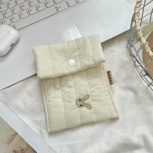 Detail of quilted bunny embroidery on a cream makeup bag with button closure