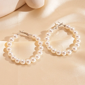 Detailed macro view of large faux pearl hoop earrings on light gold pleated silk fabric