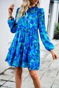 Détail de robe bleue fleurie à manches longues avec volants étagés et col montant