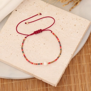 Detail of red woven bracelet with colorful beads and a white pearl on stone background