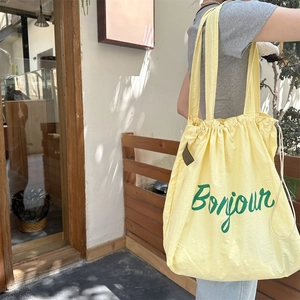 Detail of yellow canvas tote bag with green Bonjour print and drawstring closure