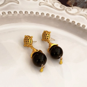 Macro view of vintage gold flower earrings with black beads on a white ceramic dish