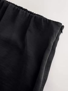 Close-up of black satin skirt featuring elastic waistband and concealed side zipper