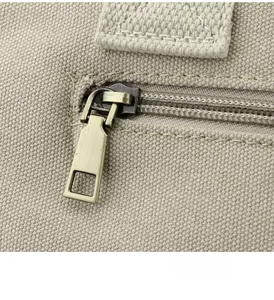 Detail of smooth bronze metal zipper and reinforced stitching on cream canvas bag