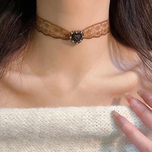 Detail of a brown lace choker featuring a resin heart charm and pearls on a model neck