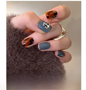 Macro shot of tortoiseshell and grey press-on nails featuring a silver cross relief