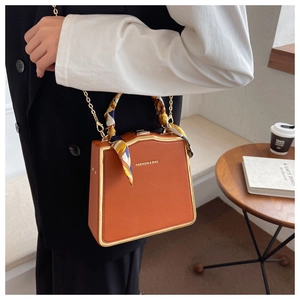 Close-up of orange vintage square handbag with gold frame and floral silk scarf handle