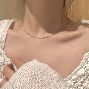 Detail of colorful beads on a gold snake chain necklace worn by a model in white lace