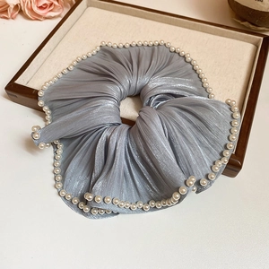 Détail d'un chouchou en tissu plissé gris avec perles blanches sur plateau de luxe