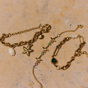 Detailed view of three gold starfish charm bracelets with colorful crystals and pearls