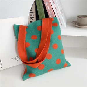 Dettaglio della borsa in maglia verde a pois arancioni su una scrivania bianca pulita