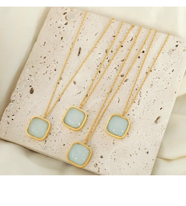 Detail of four gold square light blue gemstone necklaces on a beige textured stone base