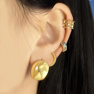 Close-up of gold C-shaped earrings and colorful zircon ear cuffs on a model ear