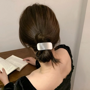 Close-up of a sleek silver rectangular metal hair tie on a low ponytail hair style