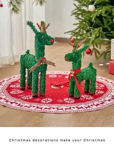 Detail of green sisal reindeer ornaments with golden antlers and festive bows on a red mat