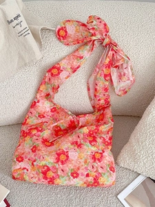Floral print shoulder bag with oversized bow strap on a soft white sherpa background