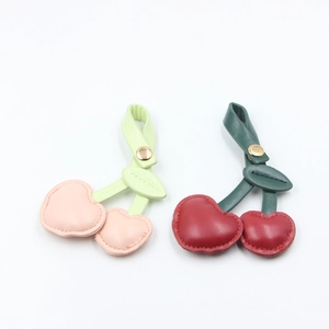 Detail showing two leather cherry pendants with metal clasps in pink and red tones