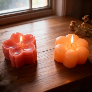 Detailed view of pink cherry blossom and orange flower handmade candles lit on a wooden windowsill
