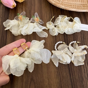 Dettaglio di orecchini a fiori in tessuto mesh con perle e cristalli su fondo legno