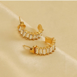 Detail view of gold U-shaped earrings with rectangular zircon stones on satin