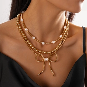 Detailed view of triple-layered gold bead necklace with pearl bow pendant on a model