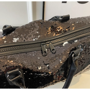 Detalle de bolso de viaje negro con lentejuelas, cremalleras dobles y asas de cuero.
