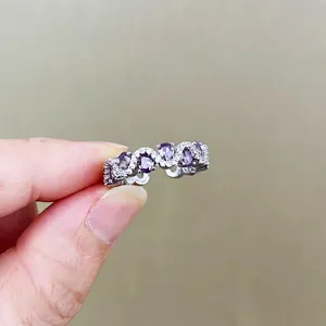 Close-up of wavy silver ring with purple oval stones and sparkling zircons on a hand