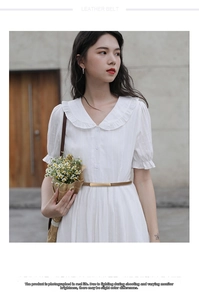 Detail of a slim tan leather belt with a gold rectangular buckle on a white dress