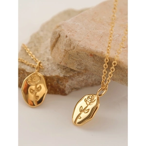 Elegant gold rose embossed oval pendant necklace set on natural stone background