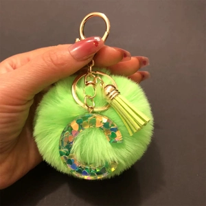 Detail of green faux fur pompom keychain with a holographic sequin letter G and gold tassel