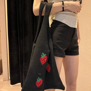 Detail of black knit tote bag featuring red strawberry embroidery and crochet texture
