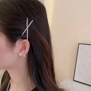Close-up of a silver rhinestone cross hair clip paired with elegant white pearl earrings
