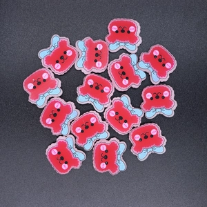 Flat lay of red resin bear charms with light blue bows on a dark gray matte surface