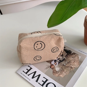 Detail of beige corduroy cosmetic bag with embroidered smiley face and zipper texture