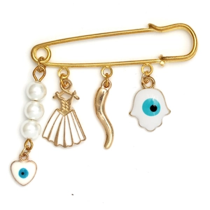 Detail of gold brooch pin featuring evil eye, pearl, heart, and dress charms on white base