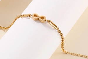 Close-up of golden infinity symbol and paperclip link chain on a neutral background