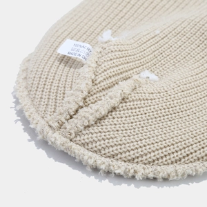 Dettaglio del berretto in maglia beige con etichetta 100% acrilico e cuciture interne