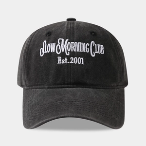 Close-up of embroidered SLOW MORNING CLUB text on a washed black cotton baseball cap