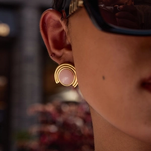 Close-up of golden multi-layered hoop earrings with pink center stone on model