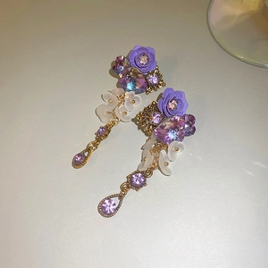 Close-up of purple floral drop earrings with crystal accents and matte white flowers