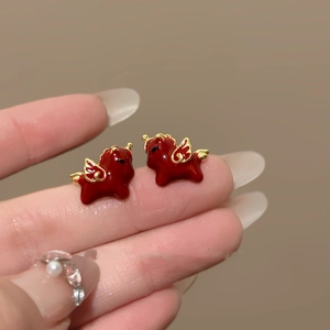 Macro view of 18k gold plated red unicorn stud earrings held on a fingertip