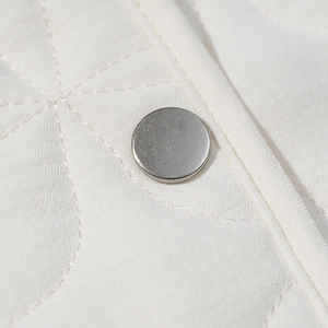 Macro shot of white diamond quilted fabric texture and silver metal snap button detail